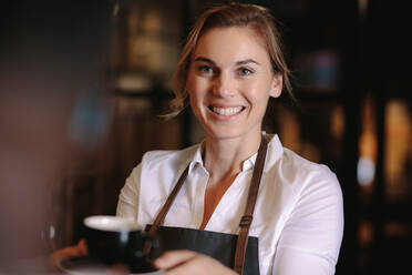 Lächelnde Frau, die Kaffee in einem Café serviert. Glücklicher Café-Besitzer, der eine Tasse Kaffee im Laden hält. - JLPSF13813