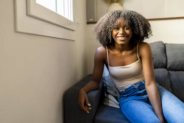 Lächelnde junge Frau sitzt zu Hause auf dem Sofa - DLTSF03246