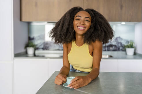 Glückliche Afro-Frau mit Kaffeetasse in der Küche - DLTSF03256