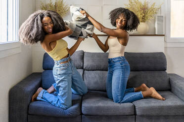 Cheerful multiracial lesbian couple doing pillow fight on sofa - DLTSF03267