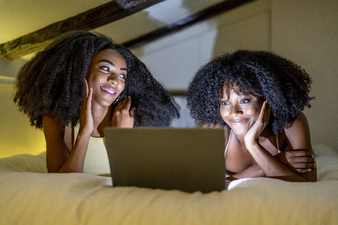 Lächelndes lesbisches Paar schaut einen Film im Schlafzimmer zu Hause - DLTSF03277