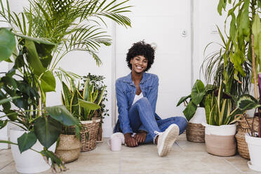 Happy young woman with coffee cup sitting amidst plants - EBBF06597