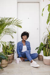 Happy woman with coffee cup sitting amidst plants - EBBF06598