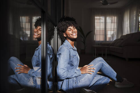 Happy young woman with eyes closed sitting in living room at home - EBBF06647