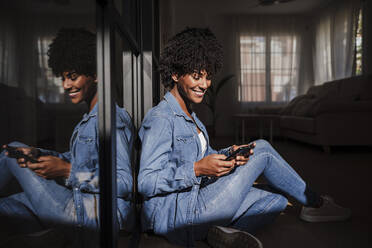 Glückliche junge Frau, die ein Smartphone benutzt und zu Hause im Wohnzimmer sitzt - EBBF06650
