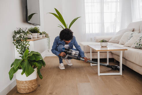 Young woman cleaning under coffee table in living room at home - EBBF06671