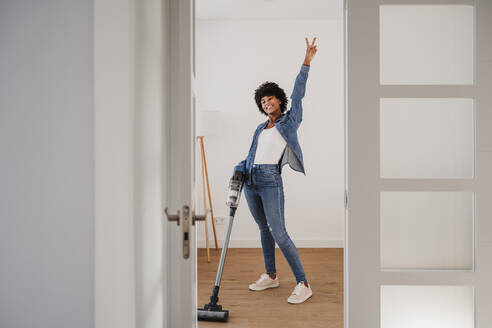 Glückliche junge Frau beim Reinigen des Wohnzimmers mit einem Staubsauger - EBBF06673