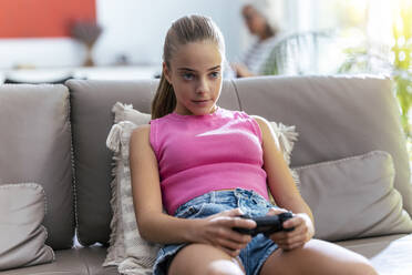 Konzentriertes Mädchen spielt ein Videospiel mit Joystick auf dem Sofa zu Hause - JSRF02225
