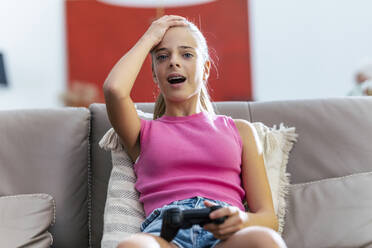 Girl with head in hand holding joystick sitting on sofa at home - JSRF02227