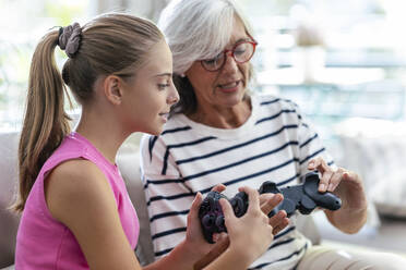 Grandmother and granddaughter talking to each other holding joysticks at home - JSRF02230