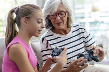 Granddaughter teaching grandmother to use joystick for playing video game at home - JSRF02231