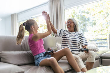 Cheerful senior woman giving high-five to granddaughter playing video game at home - JSRF02241