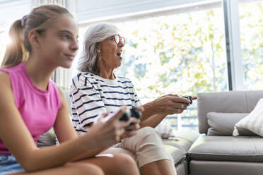 Senior woman with mouth open playing video game with granddaughter at home - JSRF02243