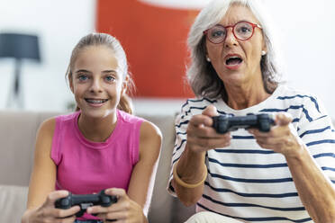 Concentrated grandmother and granddaughter playing video game with joysticks at home - JSRF02244