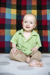 Happy cute boy sitting on carpet - EYAF02251