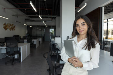 Lächelnde junge Geschäftsfrau mit Laptop am Schreibtisch im Büro - AMNF00045