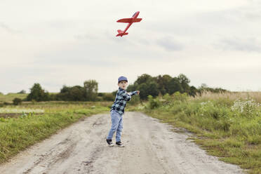 Cute boy flying toy airplane on dirt road - ONAF00178