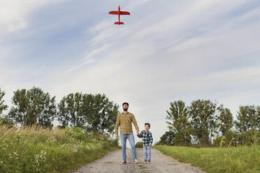 Vater und Sohn betrachten gemeinsam ein Modellflugzeug auf einem unbefestigten Weg - ONAF00184