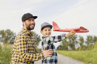 Lächelnder Vater und Sohn mit Spielzeugflugzeug in karierten Hemden - ONAF00186
