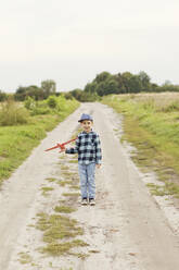 Cute boy with cap holding model airplane on dirt road - ONAF00187