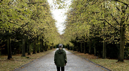 Senior woman standing on footpath amidst autumn trees - FLLF00803