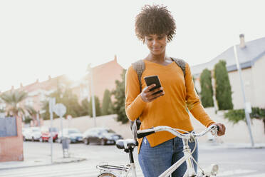 Frau mit Fahrrad, die auf der Straße ein Mobiltelefon benutzt - EBBF06685