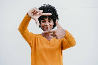 Smiling Afro woman making picture frame in front of wall - EBBF06706