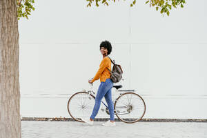 Lächelnde Frau mit Rucksack, die auf dem Fußweg Fahrrad fährt - EBBF06711