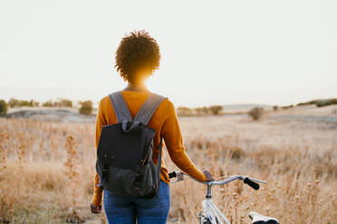 Junge Frau mit Fahrrad auf einem Feld bei Sonnenuntergang - EBBF06720