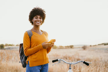 Lächelnde Frau mit Mobiltelefon auf dem Fahrrad in einem Feld - EBBF06722
