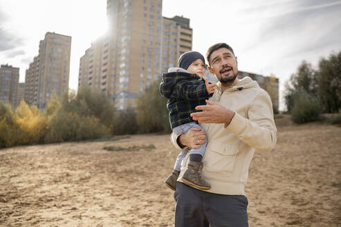 Vater mit Sohn steht vor einem Gebäude an einem sonnigen Tag am Strand - ANAF00240