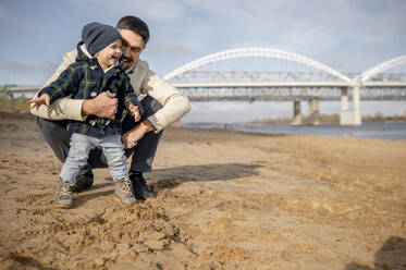 Glücklicher Vater mit Sohn am Strand an einem sonnigen Tag - ANAF00243