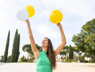 Glückliche Frau mit gelben und weißen Luftballons auf dem Fußweg - AMRF00094