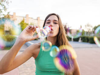 Woman blowing colorful bubbles at footpath - AMRF00100