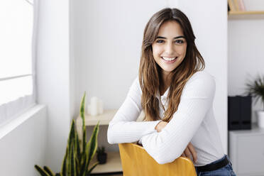 Happy woman sitting on chair at home - XLGF03104