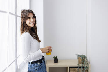 Happy woman holding coffee cup leaning on window - XLGF03118