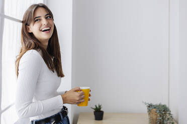 Beautiful woman holding coffee cup laughing at home - XLGF03120