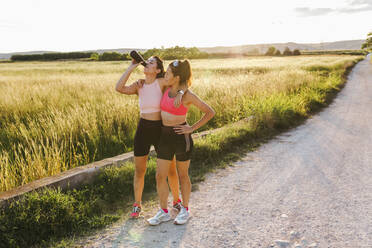 Instructor drinking water standing by woman on footpath - EGHF00601