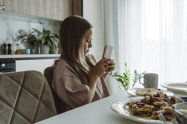 Mädchen fotografiert Frühstück auf dem Tisch mit dem Smartphone zu Hause - OSF01070