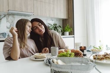 Mother embracing daughter in kitchen at home - OSF01072