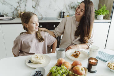 Happy woman with daughter at dining table in kitchen - OSF01073