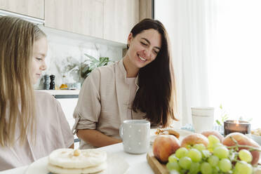 Smiling woman with daughter at dining table in kitchen - OSF01074