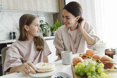 Glückliche Frau im Gespräch mit Tochter am Esstisch in der Küche - OSF01075