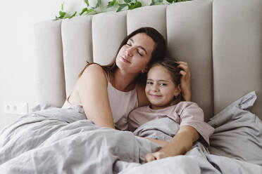 Woman with eyes closed embracing daughter lying on bed at home - OSF01084