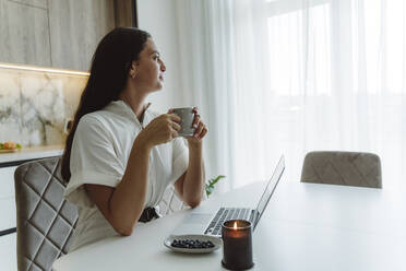 Geschäftsfrau mit Kaffeetasse und Laptop auf dem Tisch zu Hause - OSF01090