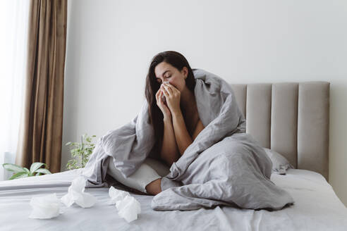 Kranke Frau schnäuzt sich mit einem Taschentuch auf dem Bett zu Hause - OSF01096