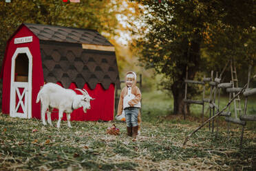 Glückliches Mädchen im Fuchskostüm neben einer Ziege auf einem Bauernhof - MDOF00119