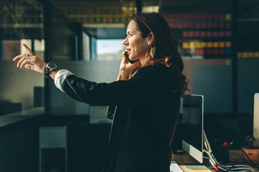 Female executive talking on mobile phone and gesturing with hand in office. Businesswoman on a phone call in office. - JLPSF13838