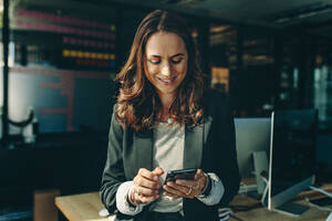 Reife Geschäftsfrau liest Text auf dem Handy im Büro. Unternehmerin benutzt ein Telefon im Büro. - JLPSF13842