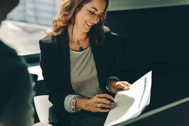 Woman entrepreneur showing a paper to her business partner while discussing business plans. Man and woman sitting in office analyzing business performance. - JLPSF13847